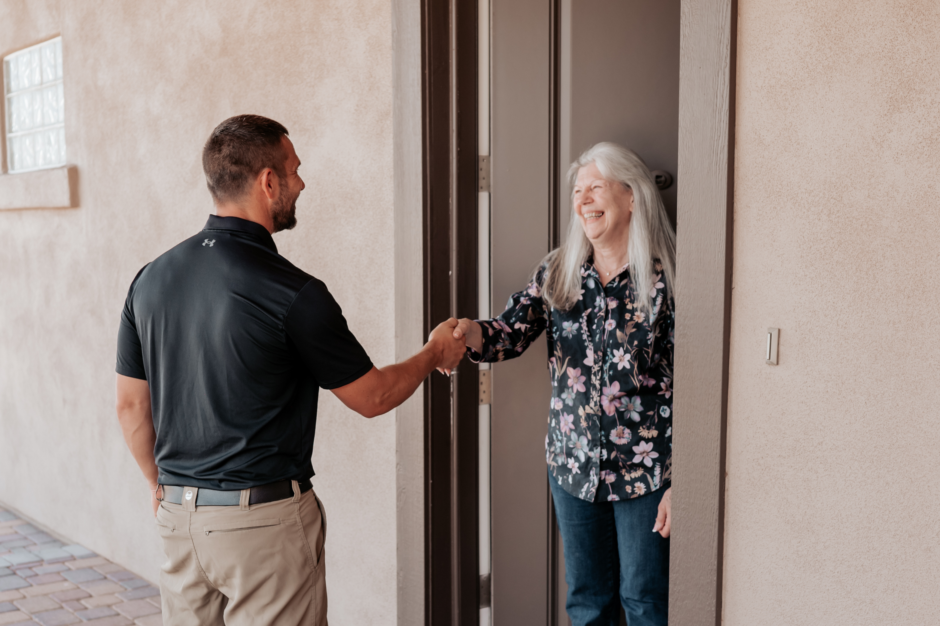Two people shaking hands and smiling at a doorway