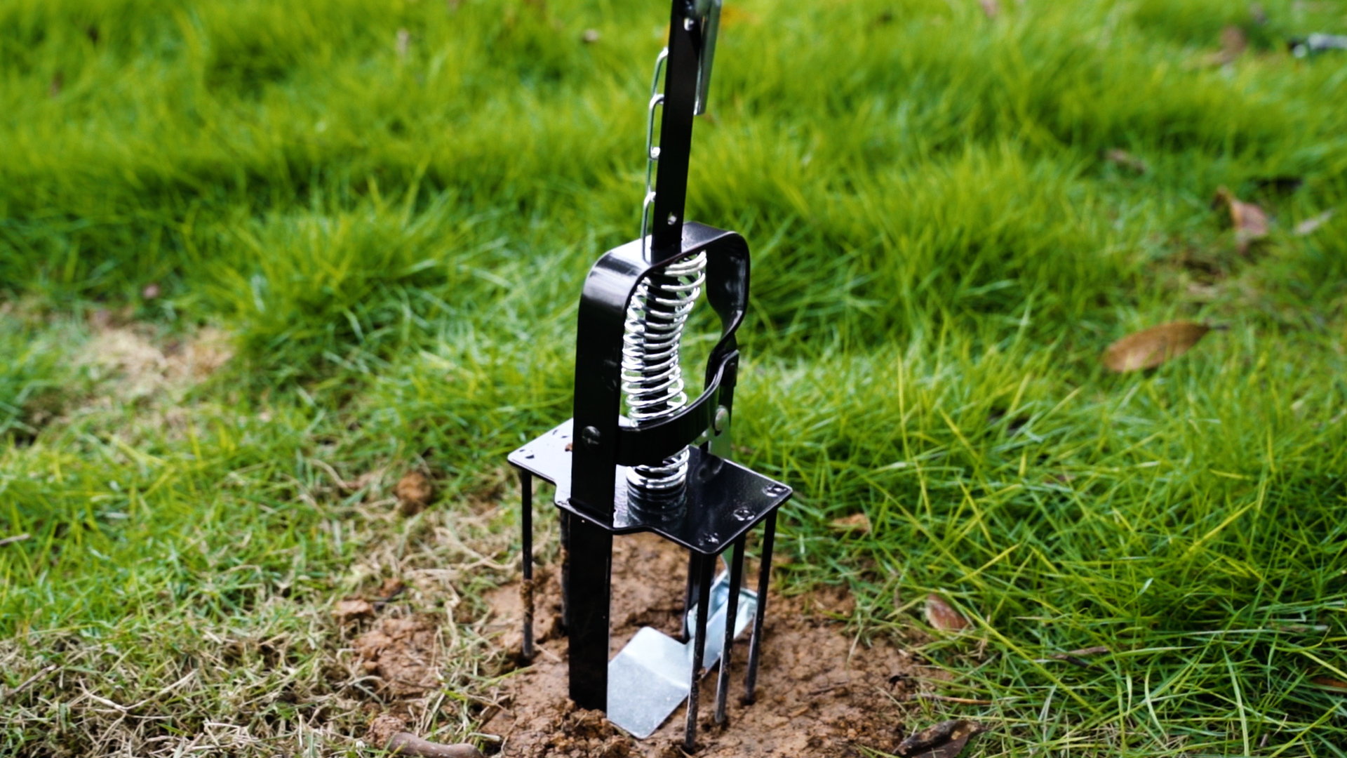 Black metal ground anchor with spring mechanism in grassy outdoor setting