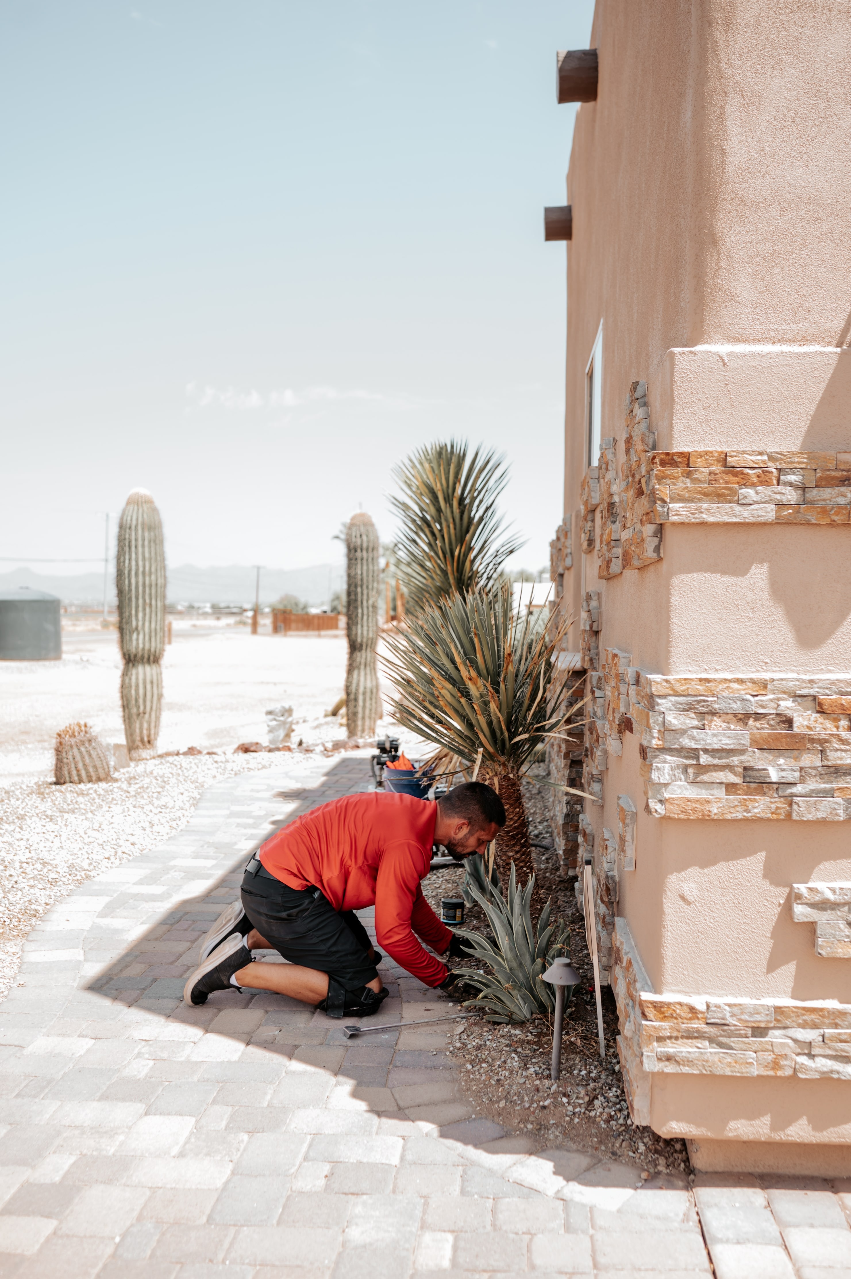 Person in red shirt working on landscaping near cacti and stone building